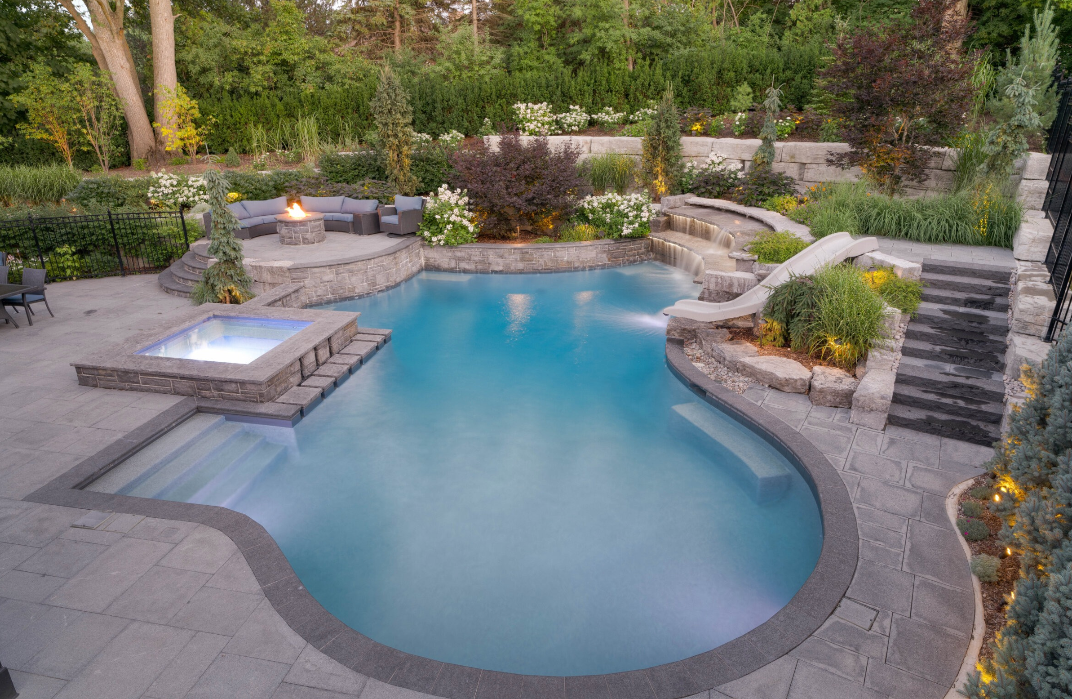 Luxury custom swimming pool with modern home backdrop and evening lighting by Emerald Isle Pools