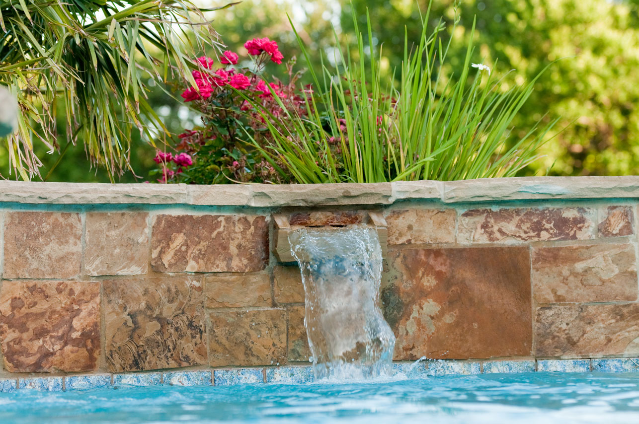 Custom pool water feature with stone wall and cascading waterfall by Emerald Isle Pools